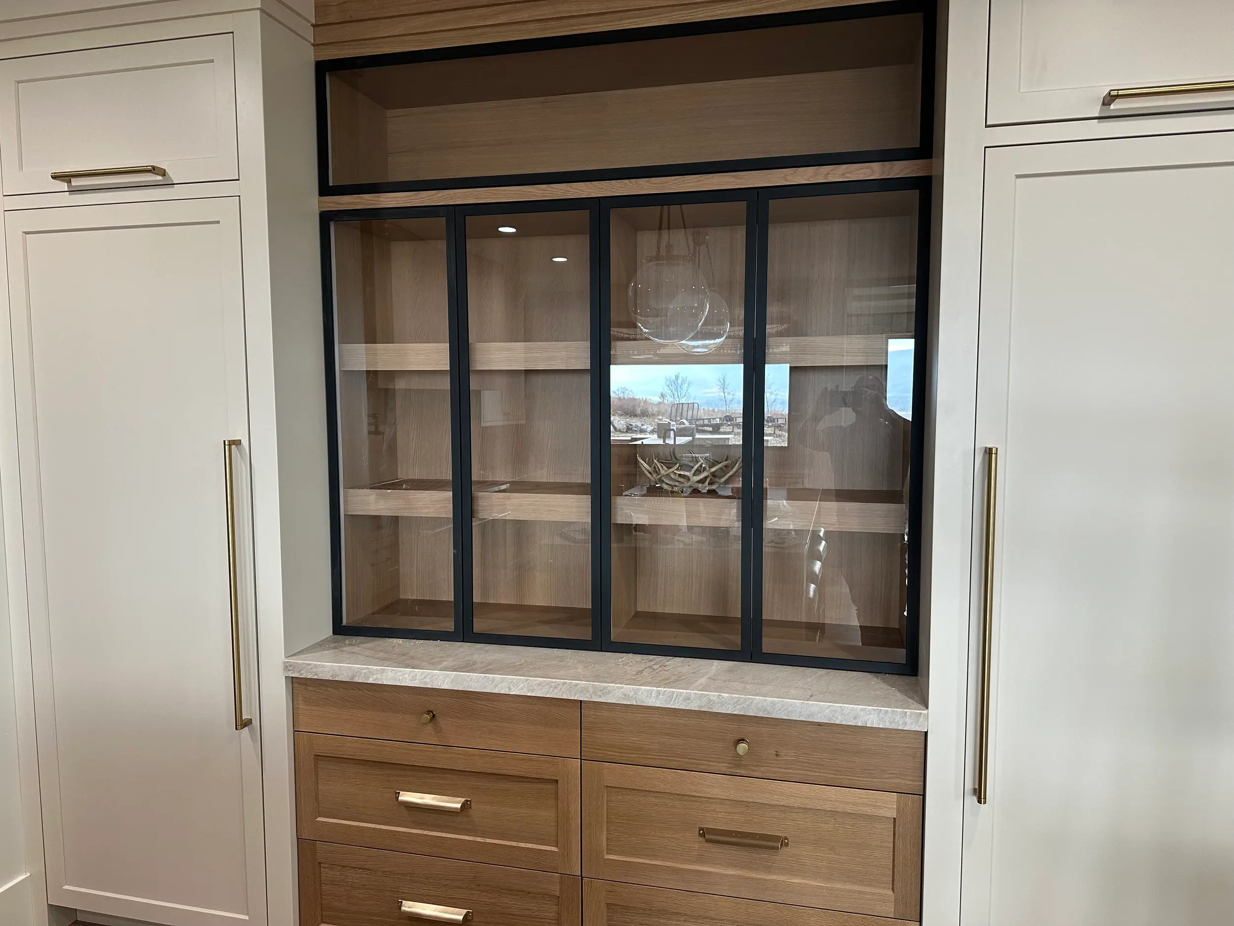 Display cabinet with oak interior shelving above quartz countertop, flanked by white shaker cabinets with gold pulls.