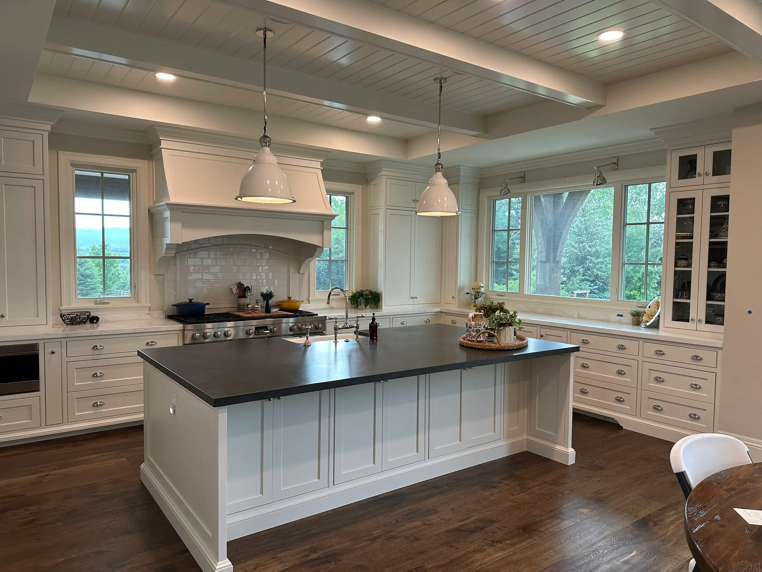 Custom white kitchen island with honed black countertop, framed by a custom-built beamed ceiling in a bespoke cabinetry project.