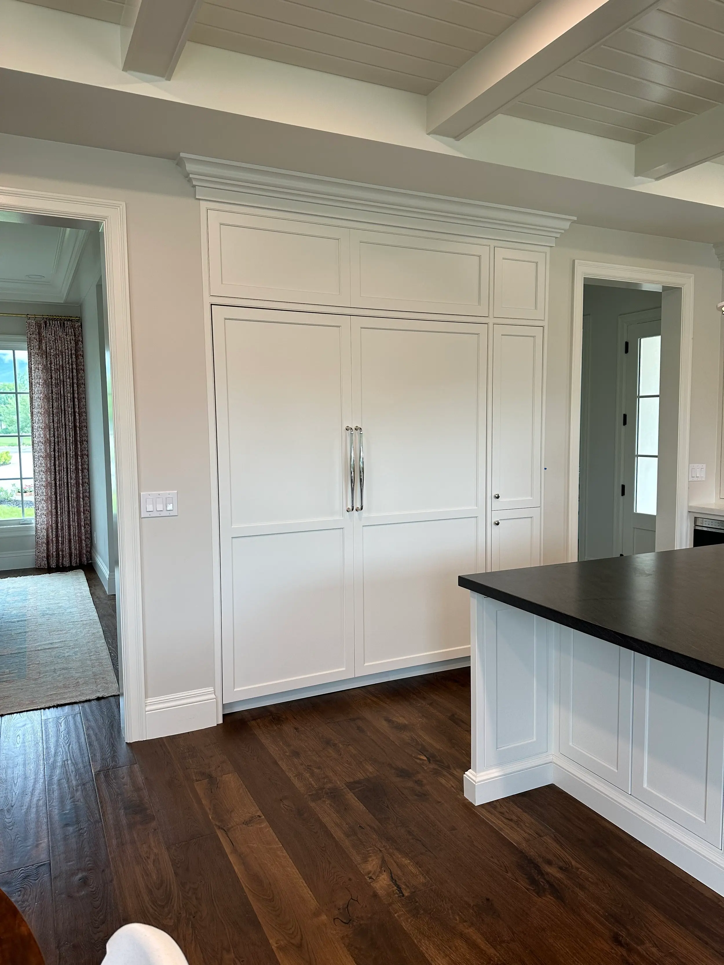 Custom paneled refrigerator built-in beneath a finished beamed ceiling, seamlessly integrated cabinetry craftsmanship.